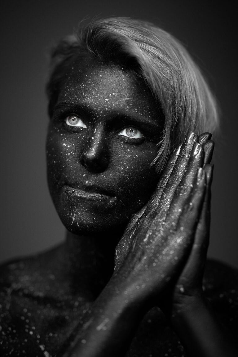 Schwarzweiß-Bodypainting-Porträt mit dunkler Farbe, hellen Augen und glitzernden Händen