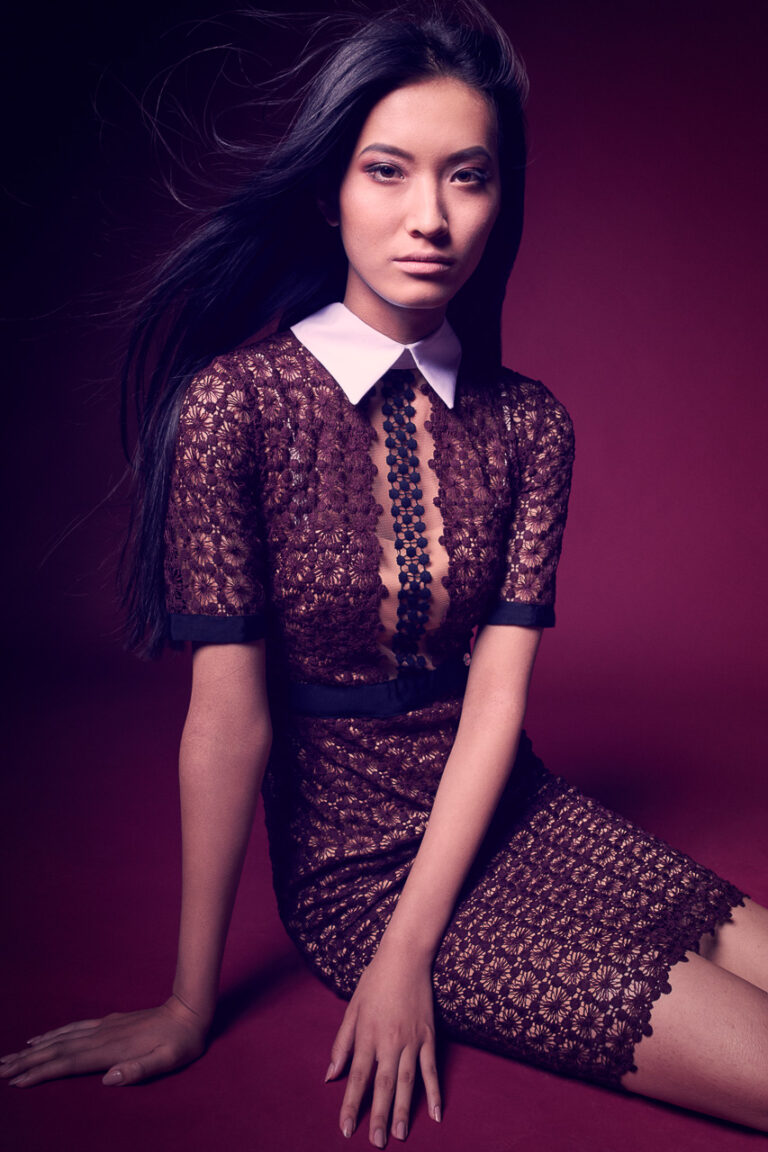 Fashion-Porträt einer Frau im dunklen Spitzenkleid mit weißem Kragen vor violettem Studiohintergrund