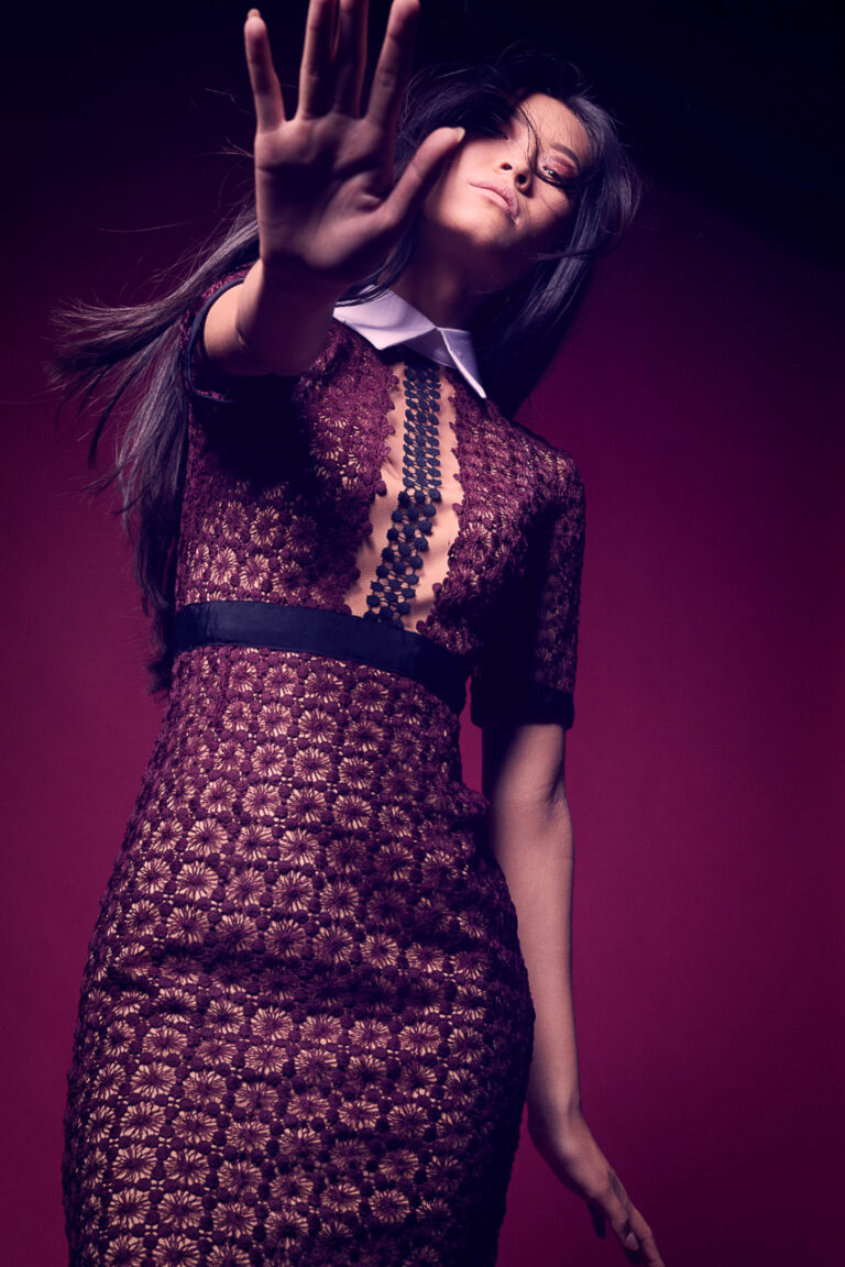 Fashion-Porträt einer Frau im dunklen Spitzenkleid mit ausgestreckter Hand vor violettem Hintergrund